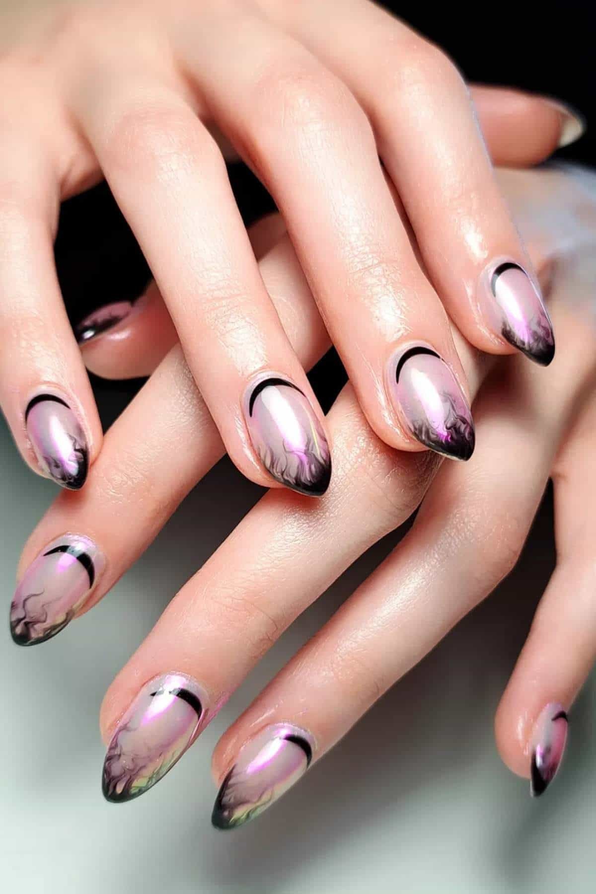 Close-up of hands with almond-shaped nails featuring pink and black ombre nail art and delicate marbled patterns.