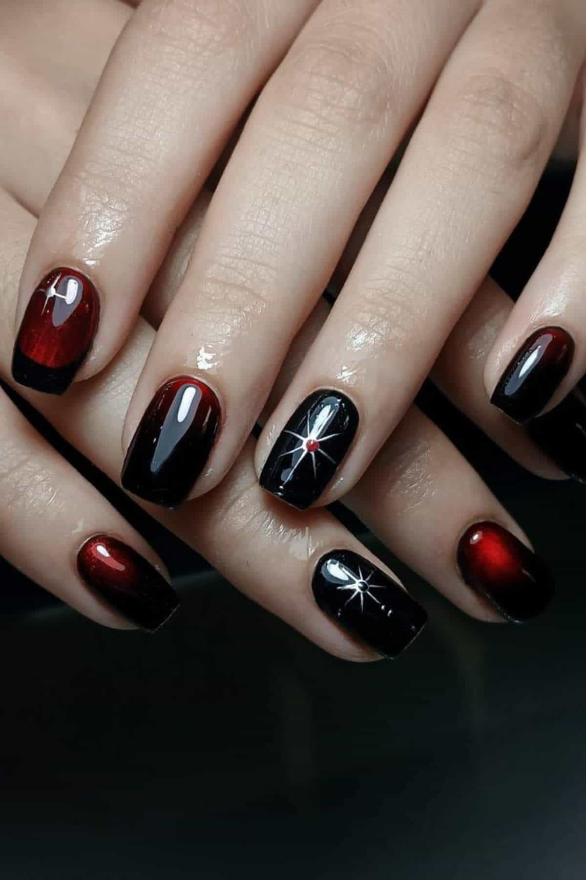 Close-up of hands with glossy red and black gradient nails, featuring white star designs on the ring fingers.